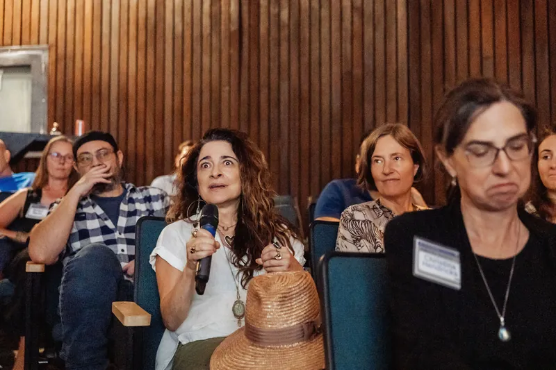 A wider view shows an attendee speaking as nearby audience members listen.