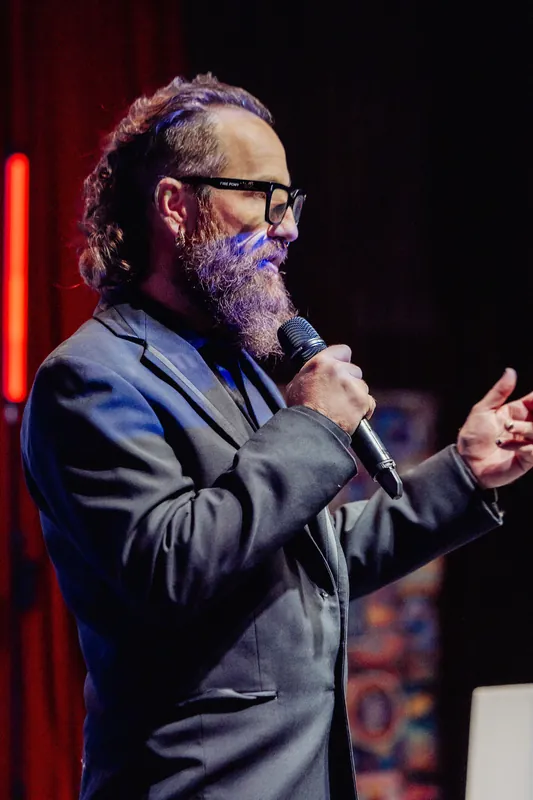 The host gestures while addressing the audience from the stage.