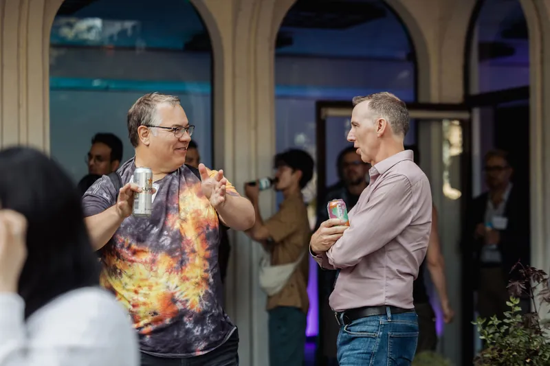 Two attendees share a light moment with drinks near an arched doorway.