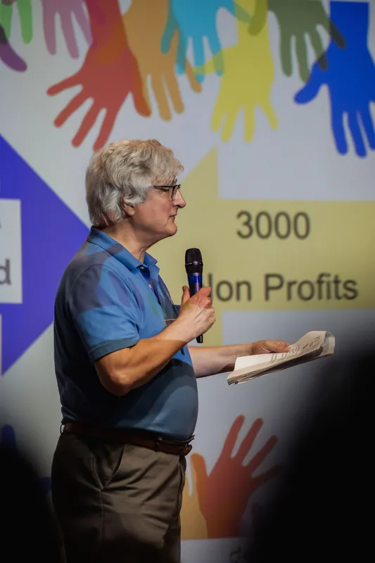 A Data for Good presenter speaks from notes beside the volunteer-impact slide.
