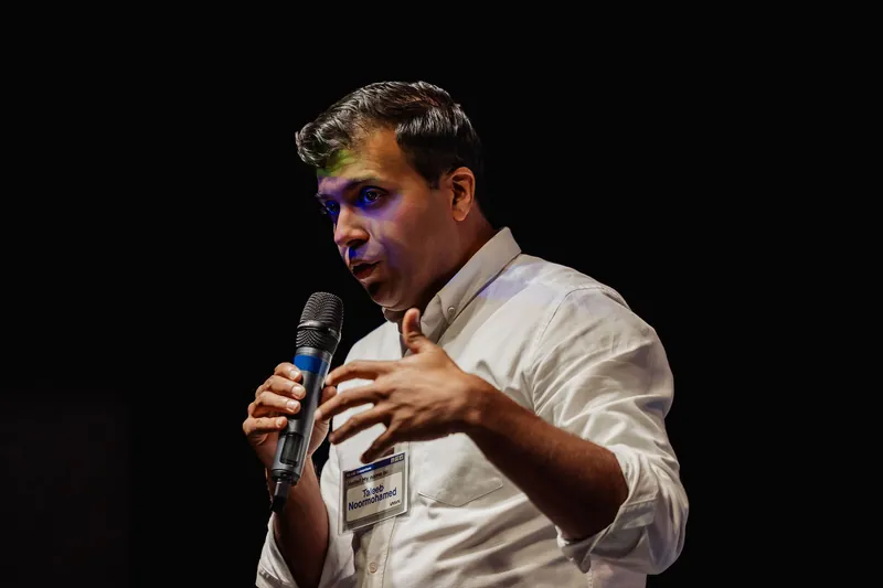 Taleeb Noormohamed leans forward and gestures while speaking.