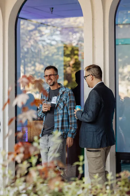 Two attendees continue their conversation near a reflective window.