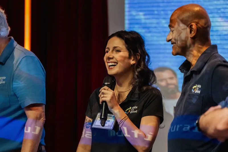 A Data for Good representative smiles while speaking into a handheld microphone.