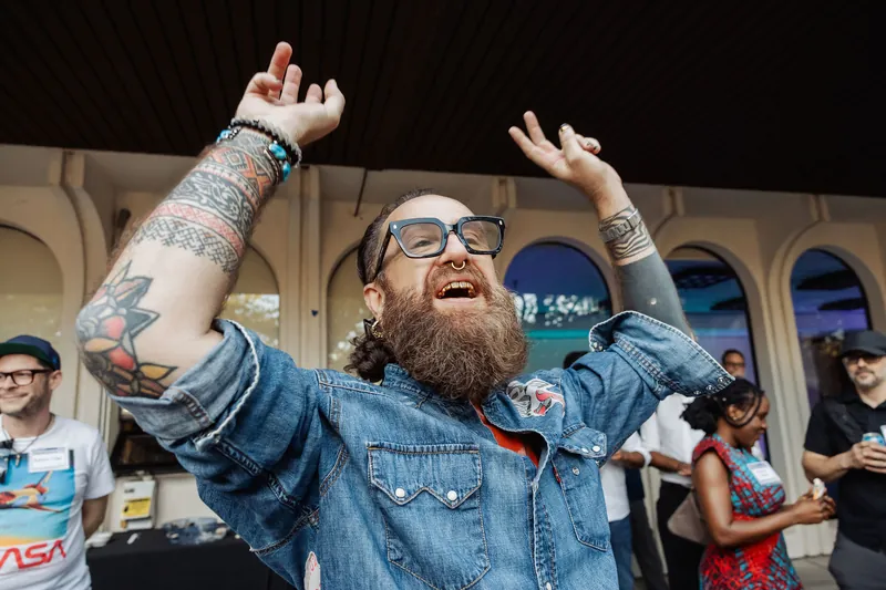 A cheering attendee raises both arms beneath the venue's arches.