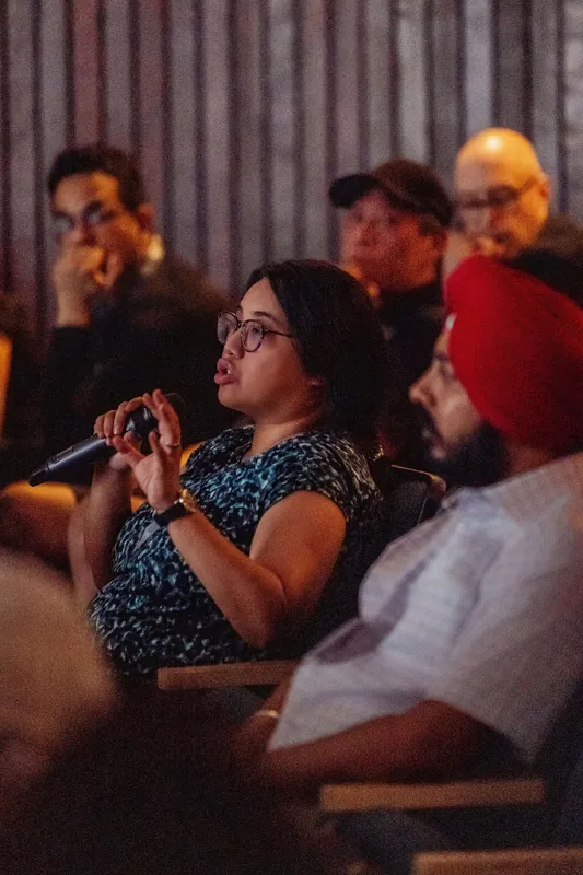 An attendee speaks into a microphone while people seated nearby listen.