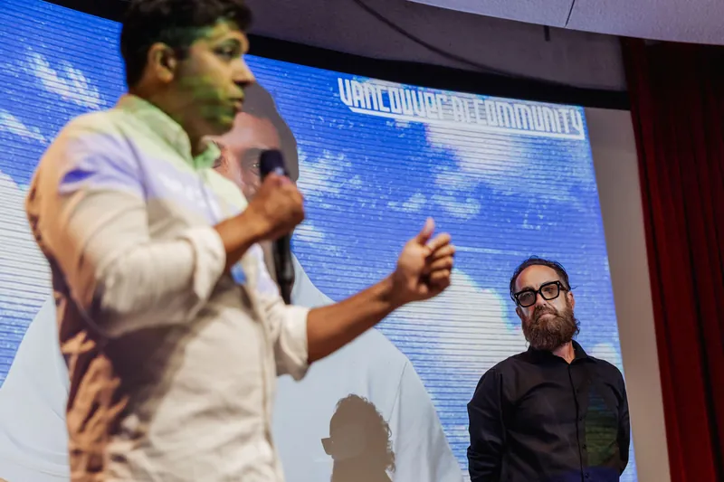 Taleeb Noormohamed speaks while the host listens behind him.