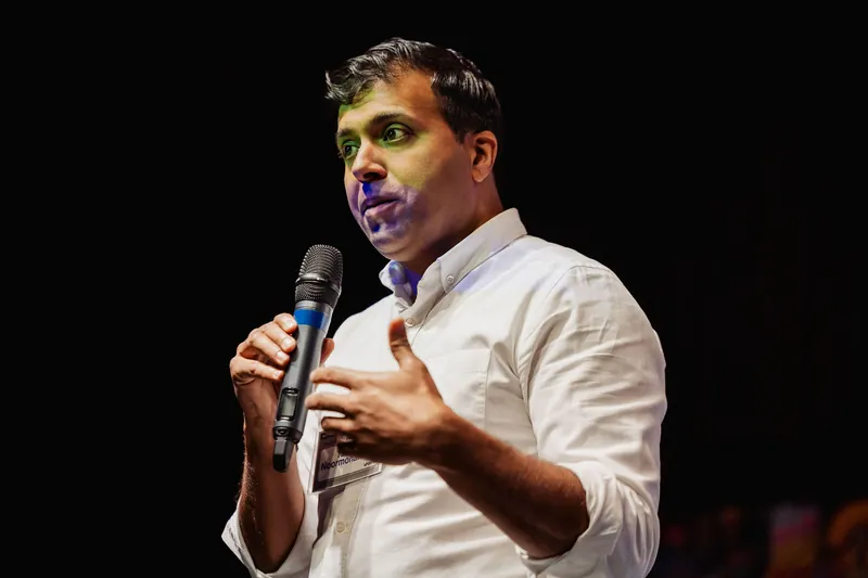 Taleeb Noormohamed speaks with his event slide visible behind him.