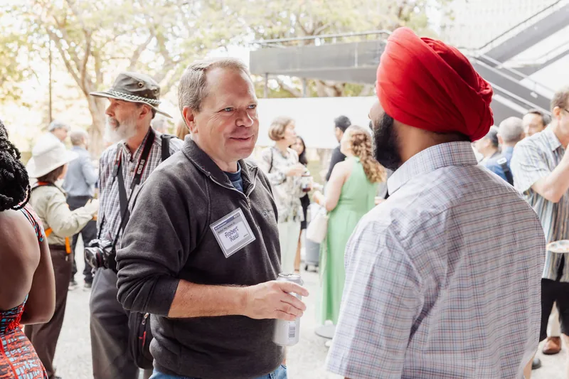 Attendees mingle with drinks in the sunlit outdoor crowd.