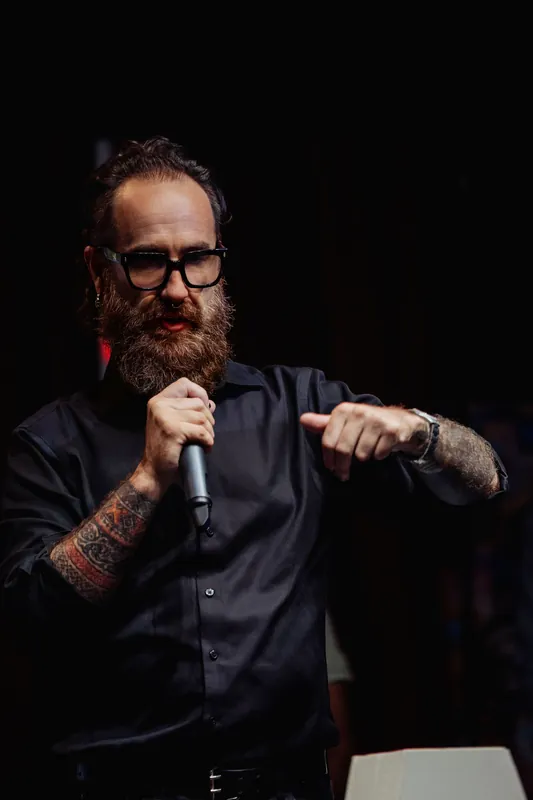 The host gestures with both hands while speaking into a microphone.