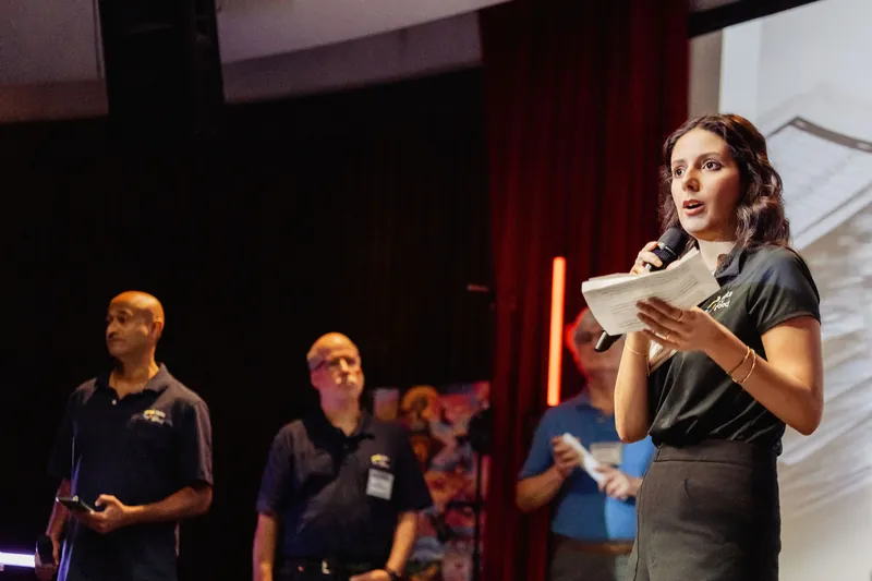 A presenter gestures with her notes as teammates wait behind her.