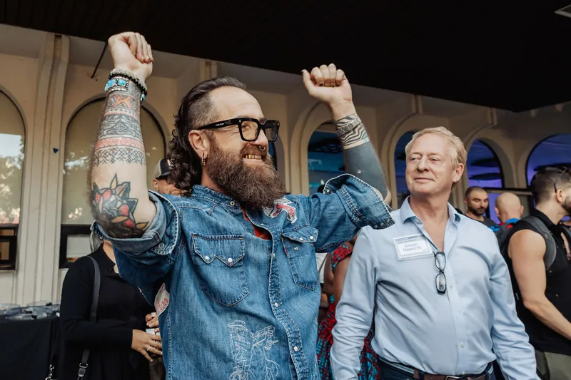 An attendee celebrates with raised arms while nearby guests smile.