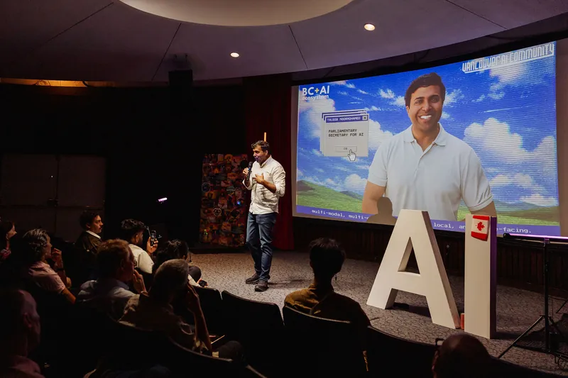 A wide stage view shows Taleeb Noormohamed speaking beneath his event slide.