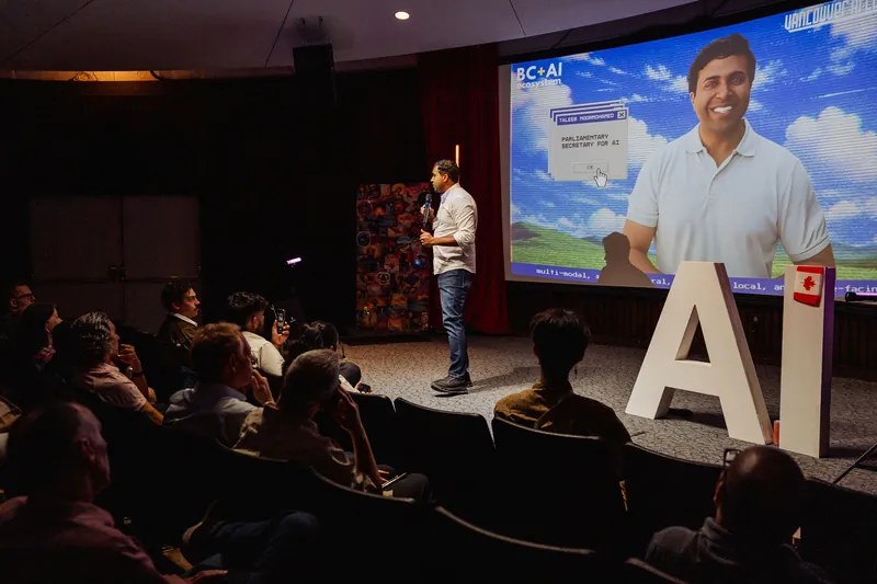 Taleeb Noormohamed addresses the front rows beneath his projected event portrait.