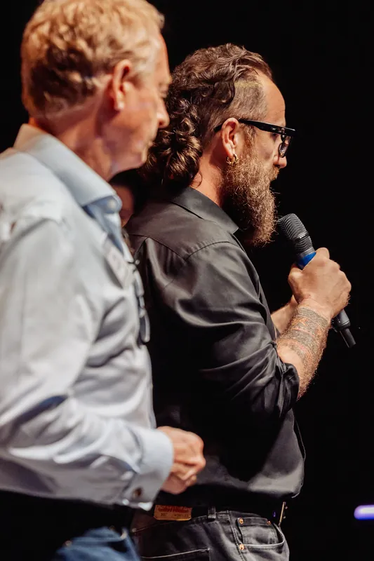 A side view shows the host continuing the onstage exchange.