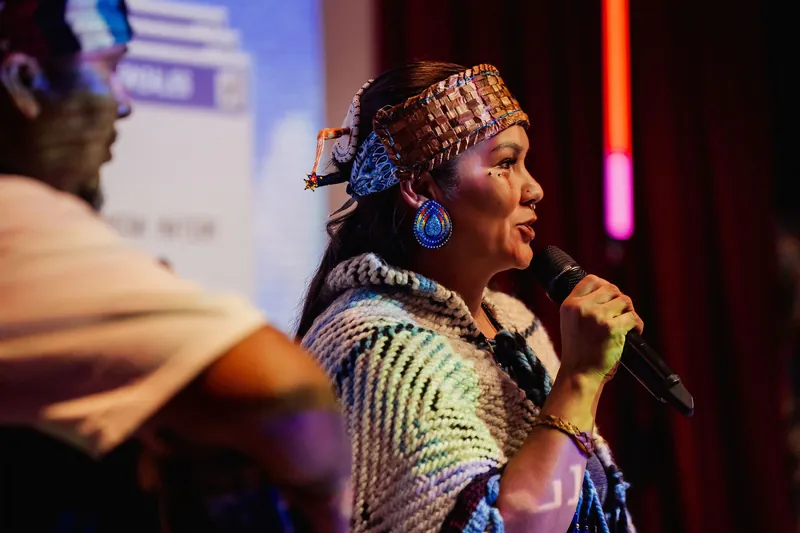 An Indigenous cultural representative speaks into a microphone during the welcome.