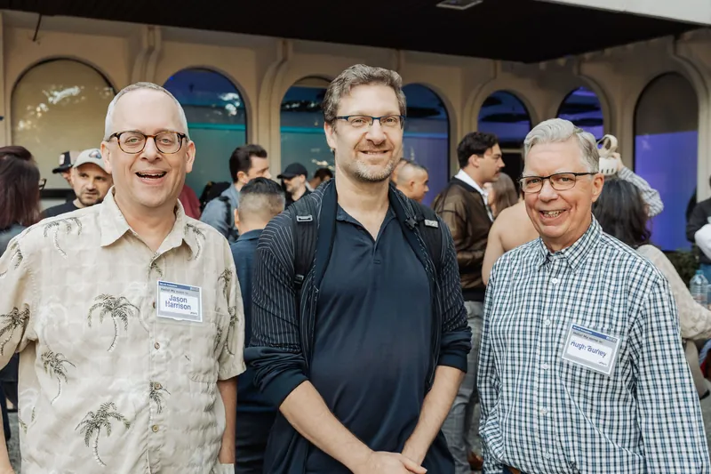 Three attendees smile together inside the arched venue entrance.