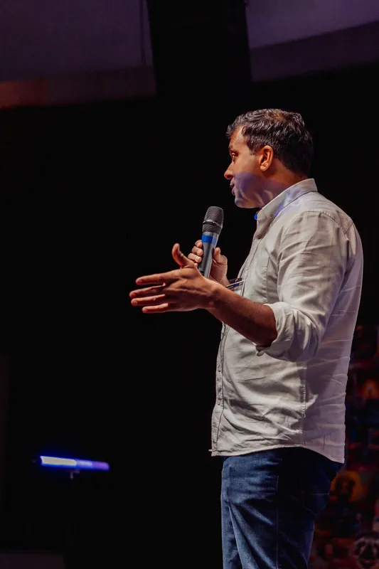 Taleeb Noormohamed speaks in profile with both hands apart.