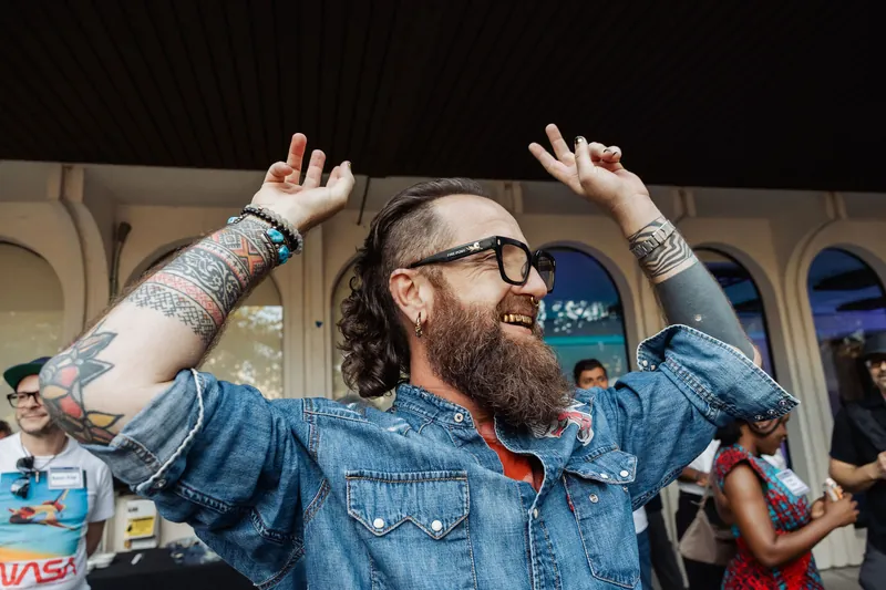 A bearded attendee throws both hands up in a playful celebration.