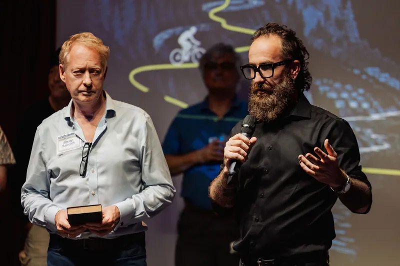 The host points across the stage during the project conversation.