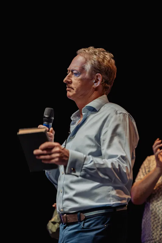 A presenter holds a book at chest height while addressing the audience.