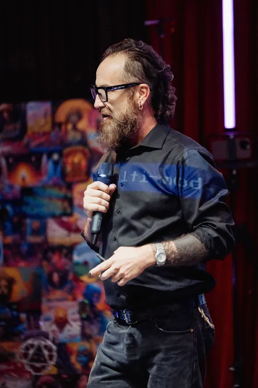 A close view captures the host's microphone and wristwatch under stage light.