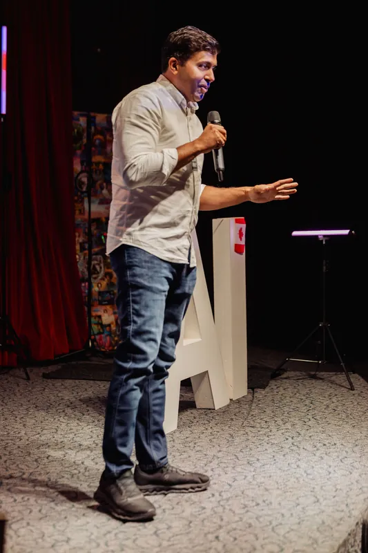 Taleeb Noormohamed speaks from centre stage in a full-length view.