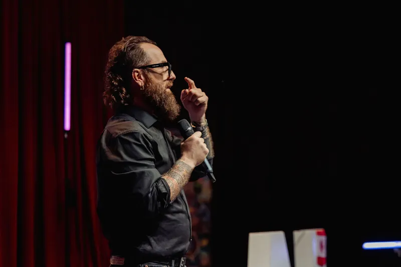 The host gestures outward while continuing the stage presentation.
