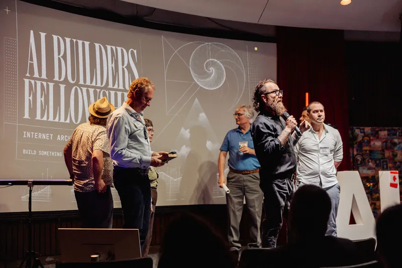 A community representative introduces the AI Builders Fellowship from the stage.