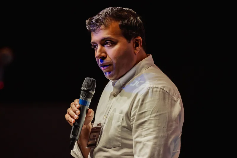 Taleeb Noormohamed pauses with the microphone held at chest level.