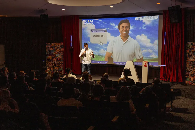 Taleeb Noormohamed stands at centre stage as the audience listens.
