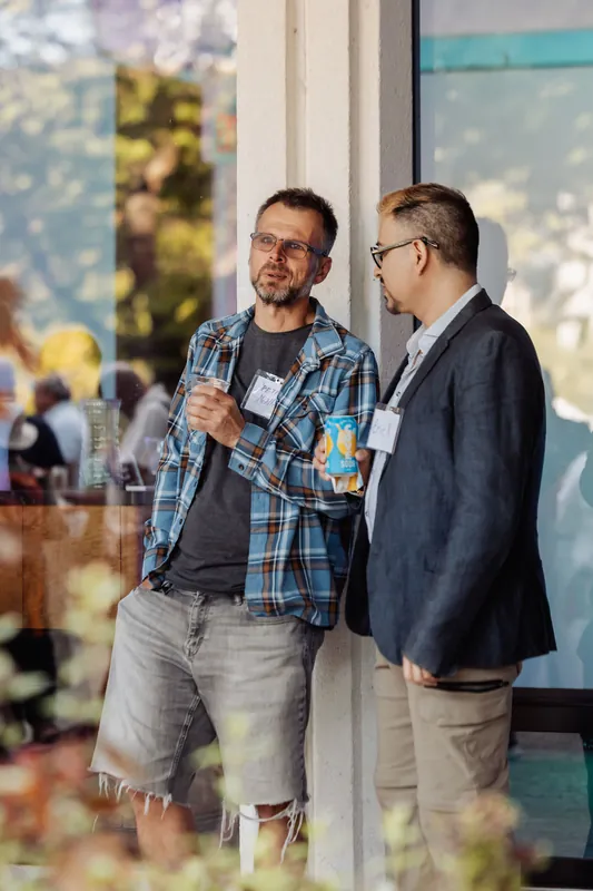 Two attendees chat with drinks beside the venue windows.