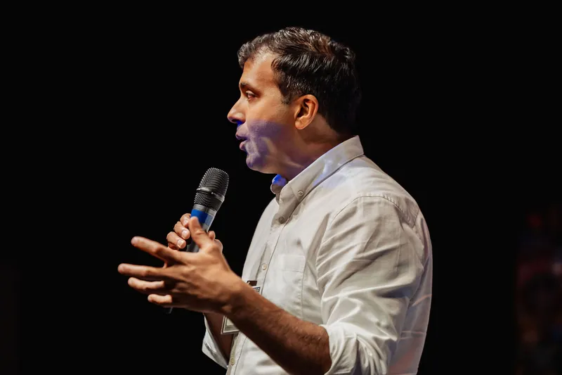Taleeb Noormohamed speaks in profile with an open-handed gesture.